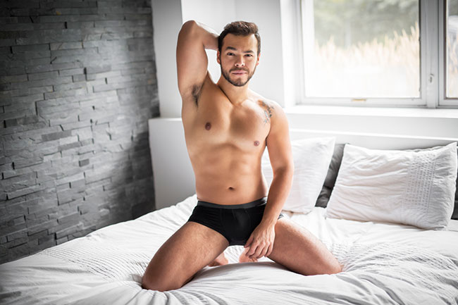 Ein junger Mann kniet in Unterhose im weißen Bett