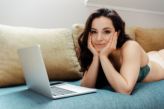 Frau liegt auf dem Bauch auf der Couch vor dem Laptop