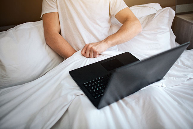Mann hält Hand unter Decke und schaut auf Laptop